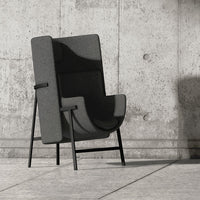 Gray upholstered chair with a sleek, minimalist design and contrasting black metal legs against a concrete backdrop.