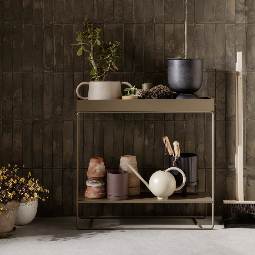 Stylish beige and earthy-toned shelf with patterned ceramic pots and greenery against a textured brown background.