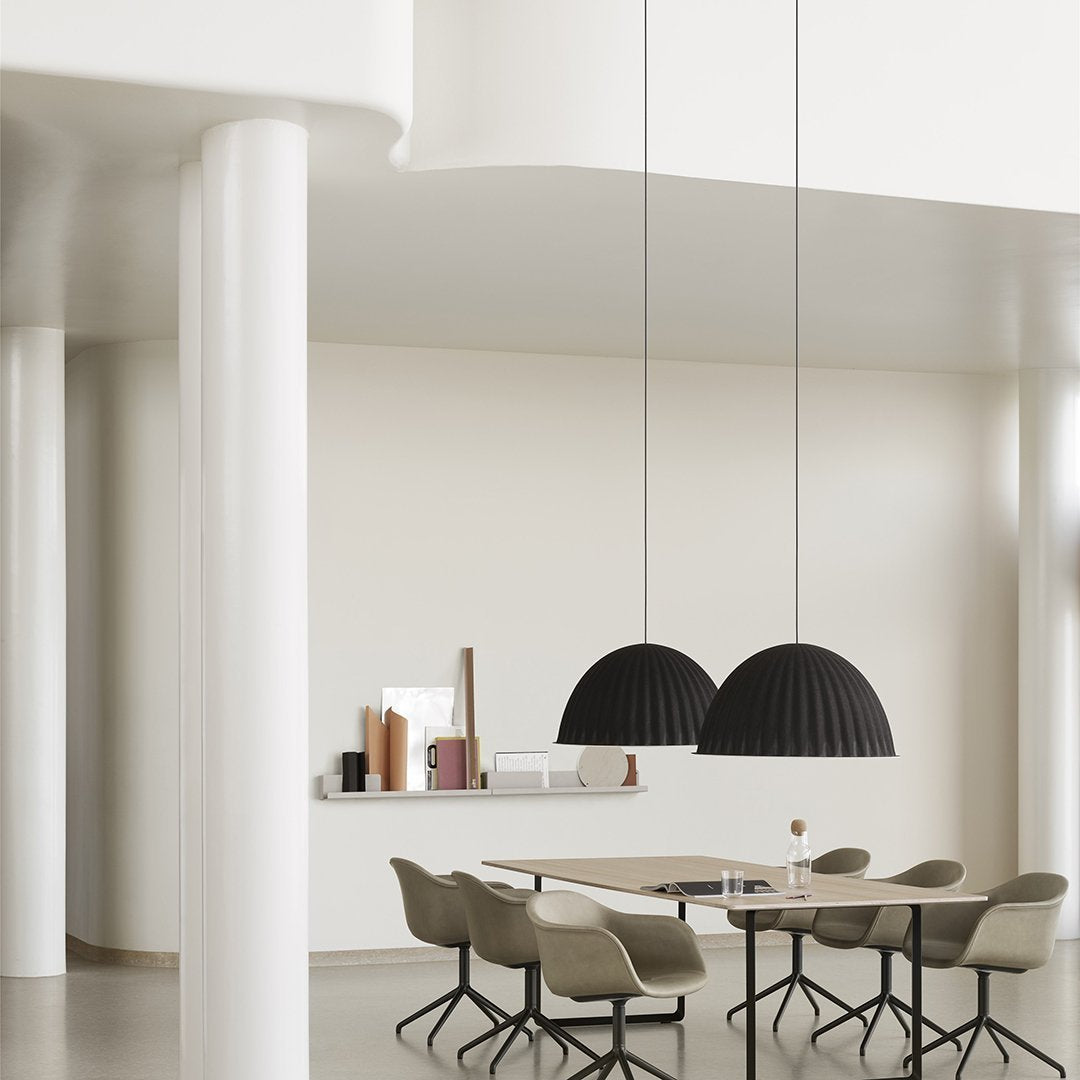 Black dome pendant lights hang above a minimalist dining table; soft, neutral tones create a modern, elegant atmosphere.
