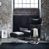 Black leather armchair with chrome accents, paired with a matching ottoman, set against a rustic stone wall and dark rug.
