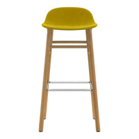 Yellow upholstered bar stool with natural wood legs and a metallic footrest, showcasing a modern, minimalist design.