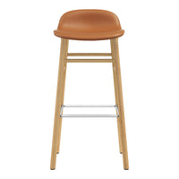 Tan leather seat with wooden legs and chrome footrest, featuring a minimalist and modern design.