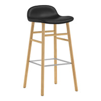 Black upholstered bar stool with natural wood legs and a sleek silver footrest. Modern design with a minimalist aesthetic.
