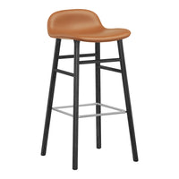 Tan upholstered bar stool with a sleek black frame and silver footrest, featuring a minimalist design.
