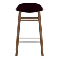 Burgundy upholstered bar stool with wooden legs and silver footrest, featuring a sleek, modern design.