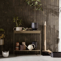 Neutral-toned console table with earthy ceramic pots and green foliage against a textured dark gray wall.