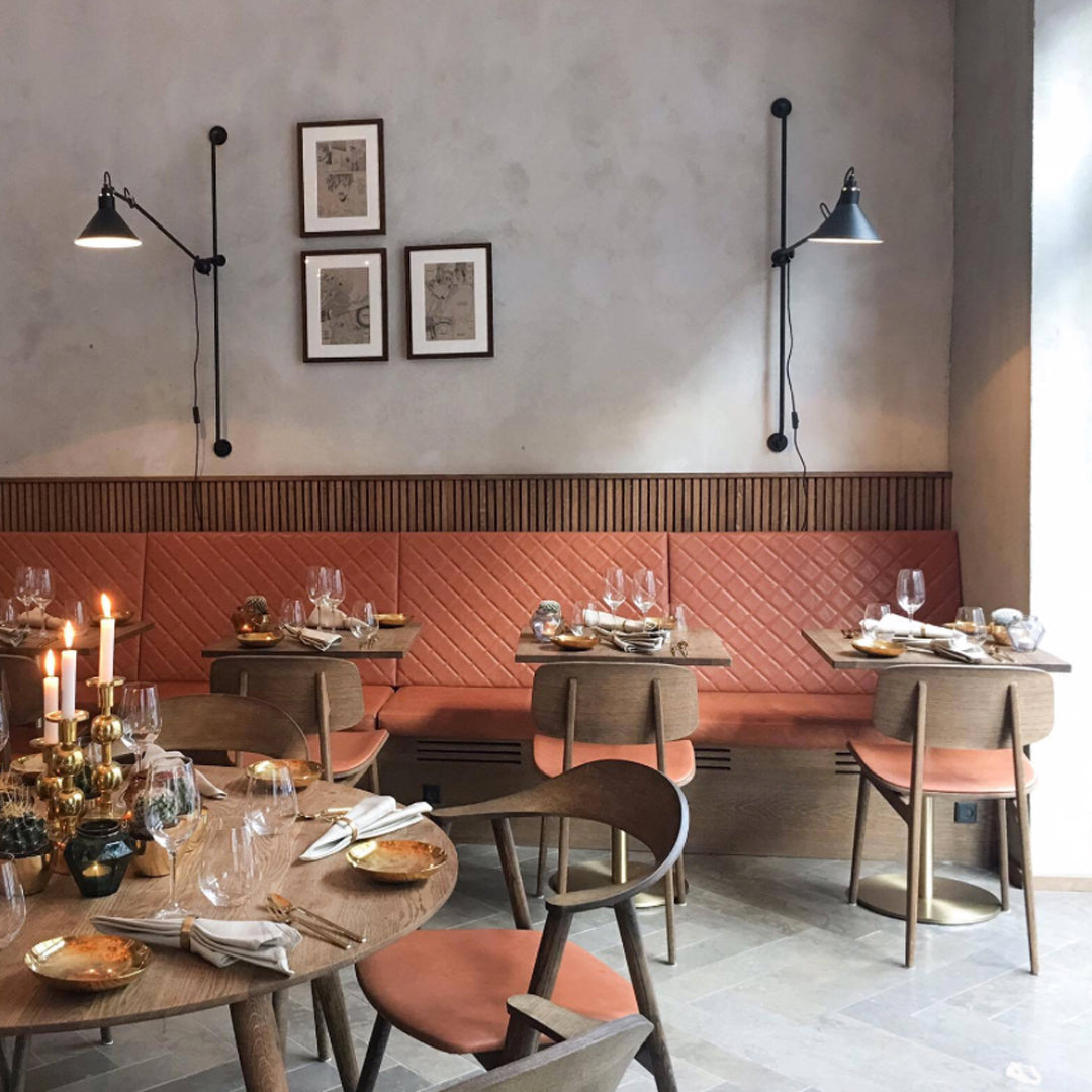 Modern restaurant interior featuring muted gray walls, textured orange upholstery, and wooden tables with soft lighting.