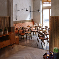 Modern restaurant interior featuring warm wood tones, orange leather banquettes, and geometric floor patterns.