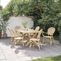 Wooden outdoor table with yellow and white striped chairs, surrounded by lush greenery and gray stone patio.
