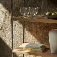 Wooden shelves displaying earthy tones, clear glassware, and decorative books with subtle colors. Warm, natural textures and shadows.