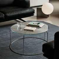 Round glass coffee table with striped pattern, black metal frame, and a dark blue rug in a modern living room setting.