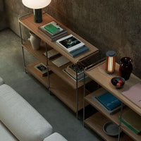 Wooden shelf with light wood finish, black accents, and a mix of green, blue, and pink books and decorative items.