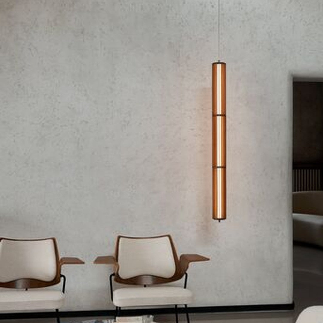 Sleek vertical pendant light in warm amber tones against a modern textured wall, complemented by minimalist white chairs.