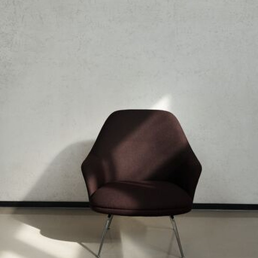 Modern dark brown upholstered chair with smooth texture and minimalist design against a light gray wall.