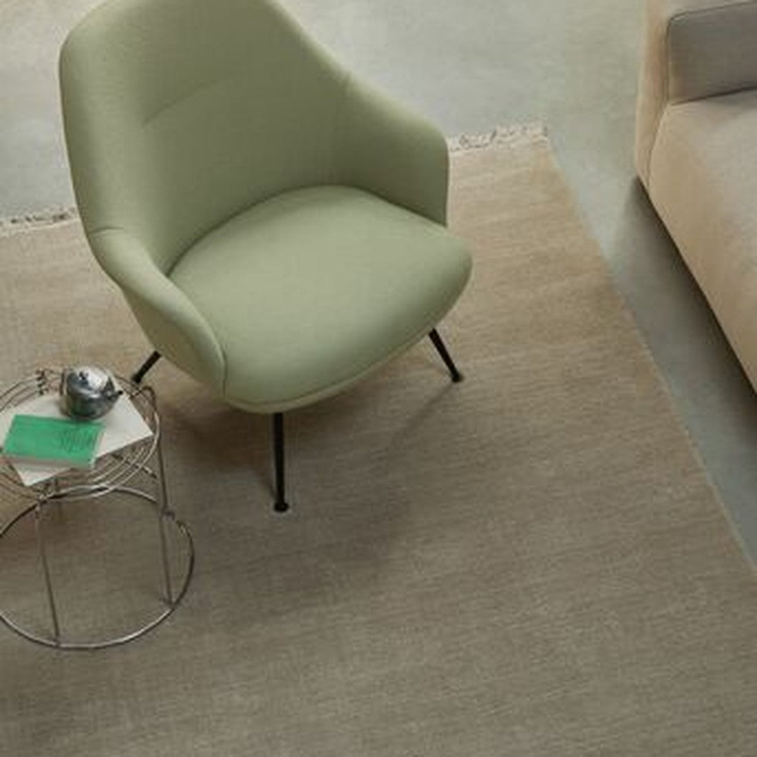Green upholstered chair on a neutral beige rug, complemented by a metallic side table and contemporary decor.