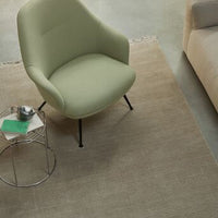 Green upholstered chair on a neutral beige rug, complemented by a metallic side table and contemporary decor.
