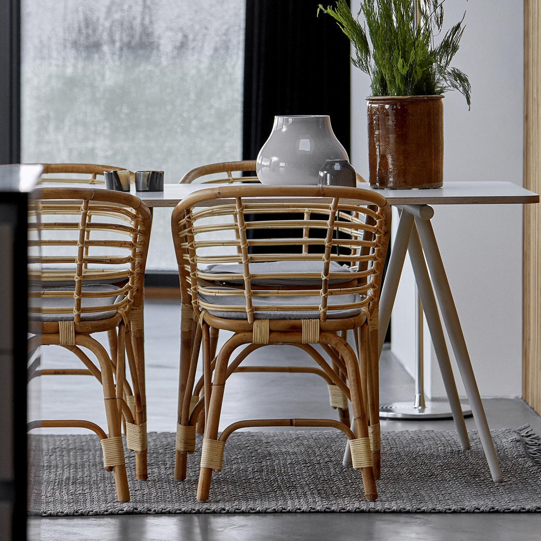 Woven rattan chairs in natural tones with a grey rug, accompanied by sleek white table and ceramic vase.