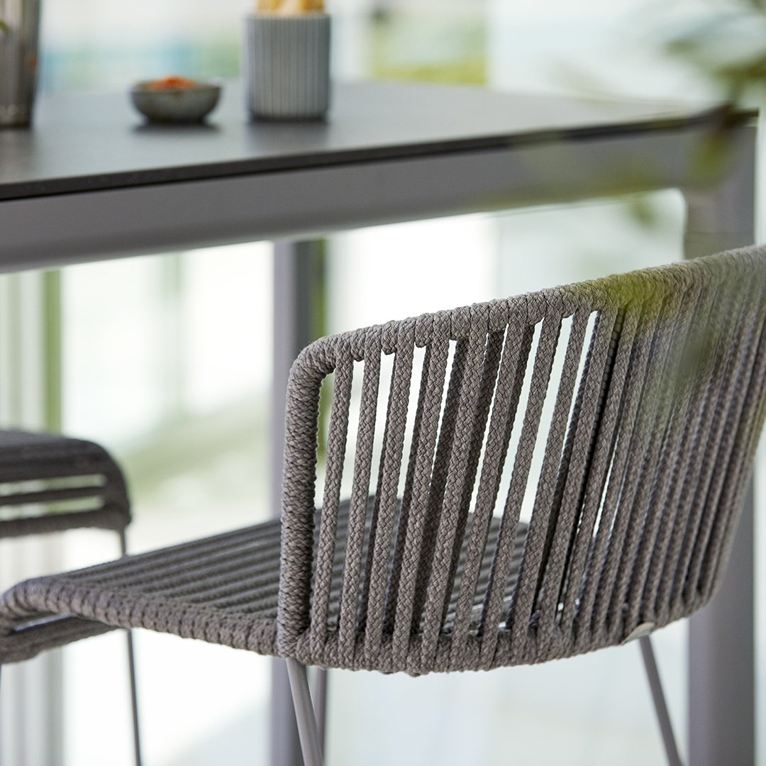 Gray woven dining chair with sleek lines, set against a minimalist backdrop. Perfect modern accent for any space.