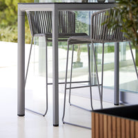 Stylish gray bar stools with sleek woven patterns, paired with a modern minimalist table in a bright, airy setting.