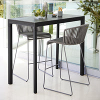 Black table with sleek lines, paired with gray woven bar stools for a modern, understated look in any setting.