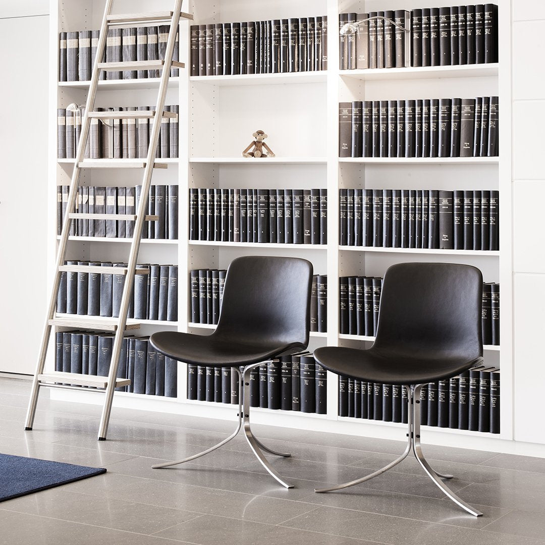 Two sleek black chairs with a minimalist design, set against a backdrop of white shelves and dark book spines.