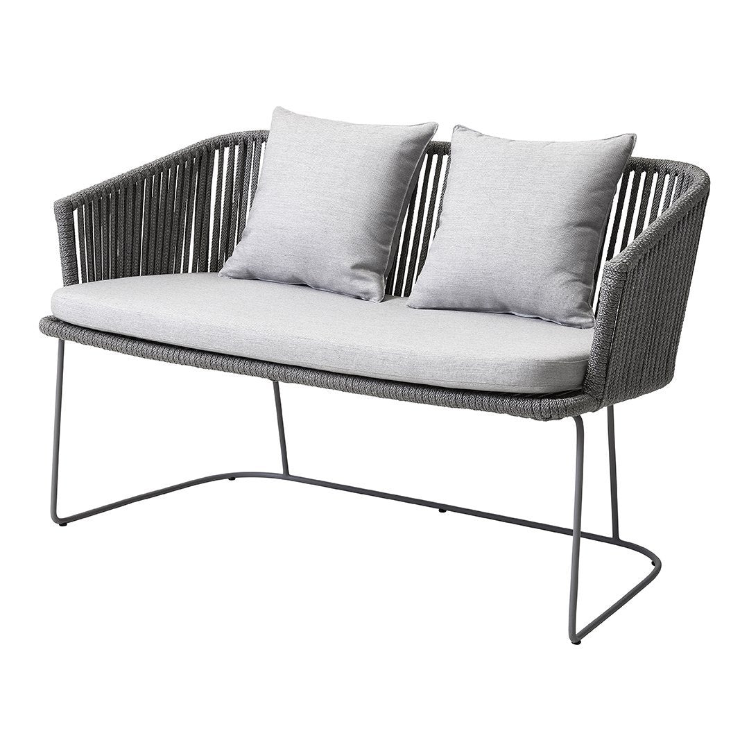Gray wicker loveseat with light gray cushions, featuring a modern design and sleek metal legs. Perfect for outdoor decor.
