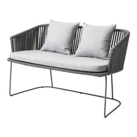 Gray wicker loveseat with light gray cushions, featuring a modern design and sleek metal legs. Perfect for outdoor decor.