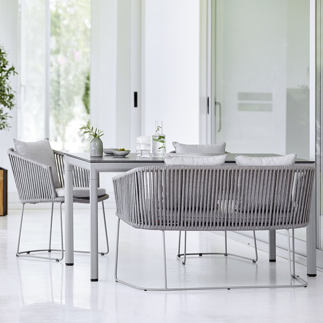 Stylish outdoor dining set featuring gray woven chairs and a sleek gray table, set against a minimalist bright backdrop.