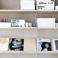 Neutral-toned shelves display white boxes, copper accents, and black-and-white magazine covers for a minimalist aesthetic.