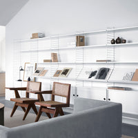 "Modern living room featuring a neutral color palette with white shelves, brown wooden chairs, and a gray sofa."