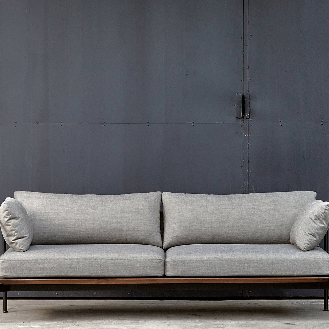 Gray upholstered sofa with two round cushions, set against a dark metal backdrop. Modern minimalist design.