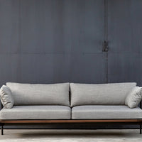Gray upholstered sofa with two round cushions, set against a dark metal backdrop. Modern minimalist design.