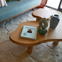 Light wood coffee table with natural curves, green decor accents, and textured beige rug for a warm, inviting atmosphere.