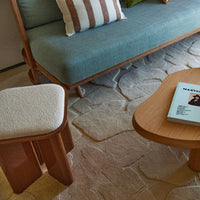 "Pastel blue sofa with striped pillows, textured cream stool, and warm wood coffee table on a light stone-patterned rug."