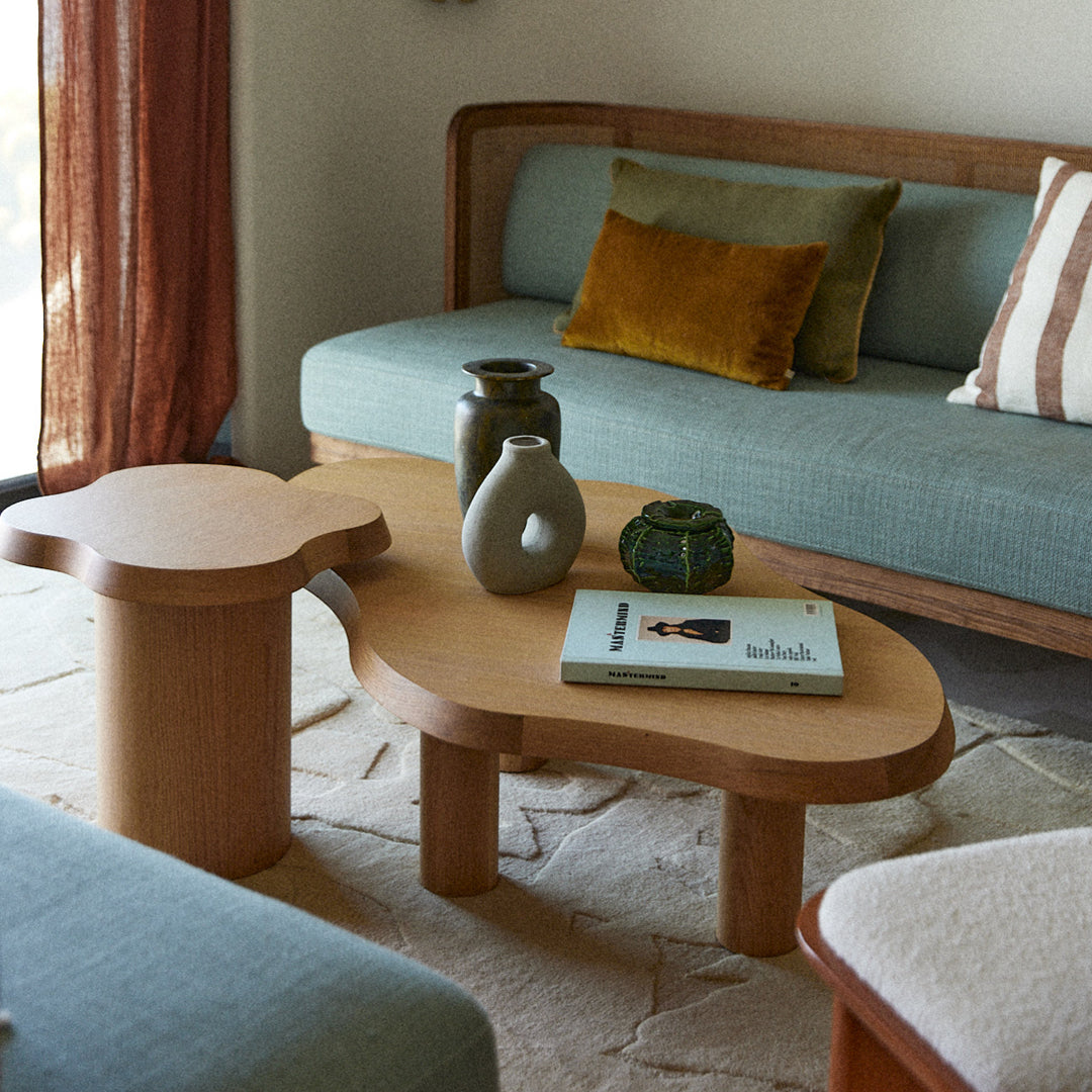 Light wood coffee table with a soft organic shape, paired with teal and earthy accent pillows in a cozy living room setting.
