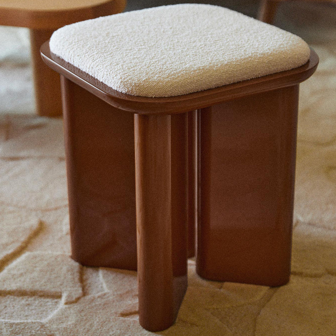 Brown wooden stool with a cream-textured cushion, modern design on a light-colored patterned rug.