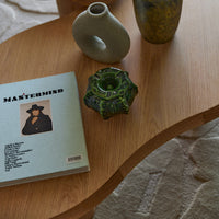 "Green ceramic vase with intricate patterns, gray stone vase, and a light blue book on a wooden table."