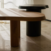 Natural wood tone table with smooth, rounded edges and a contrasting sleek black cylindrical base. Modern minimalist design.