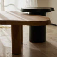 Natural wood and sleek black modern table with curved edges, featuring minimalist design and contrasting tones.