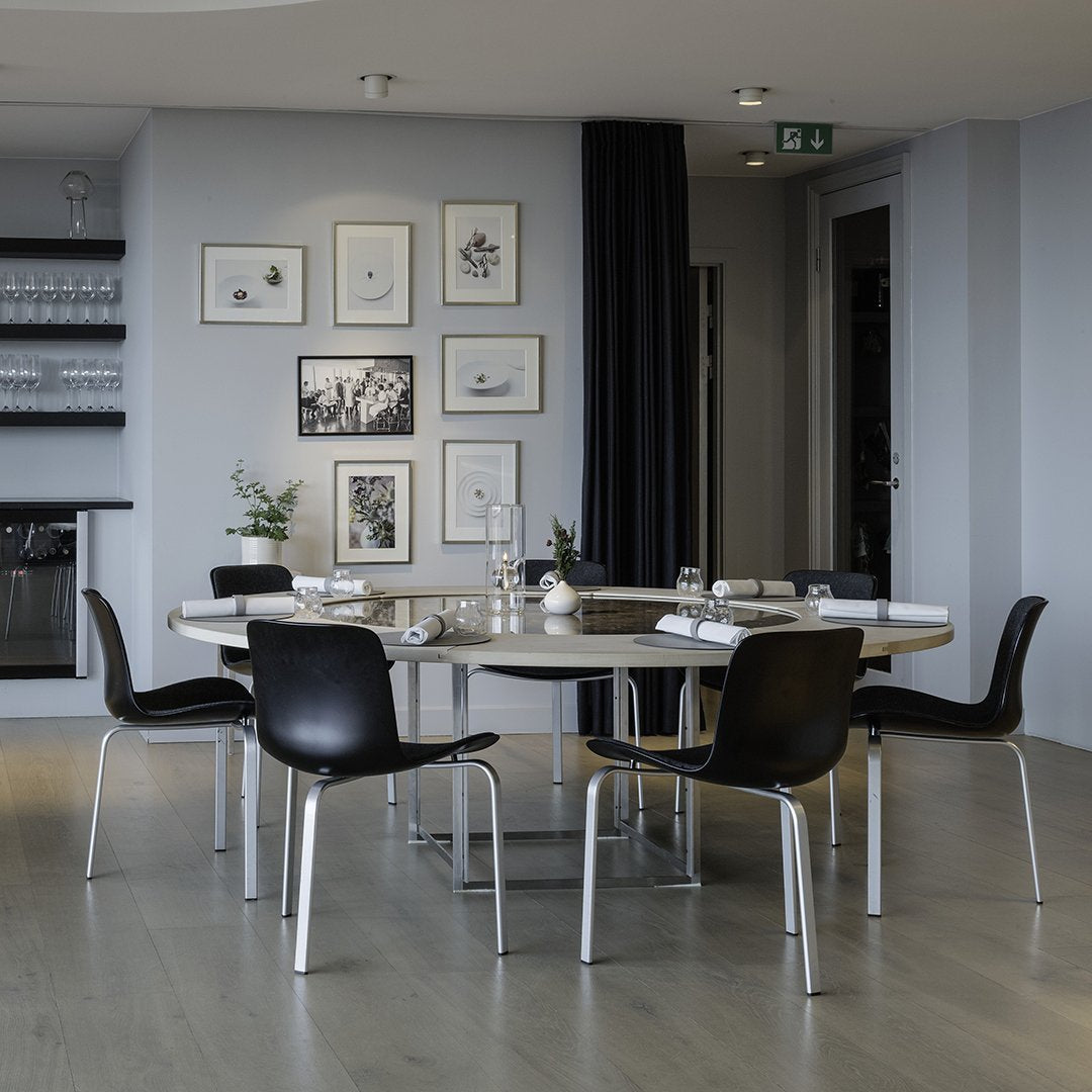 Modern black dining chairs contrast against a light wooden table in a stylish grey interior with framed art.