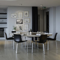 Modern black dining chairs contrast against a light wooden table in a stylish grey interior with framed art.