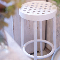 White bar stool with a round, perforated seat and slender legs, perfect for modern decor.