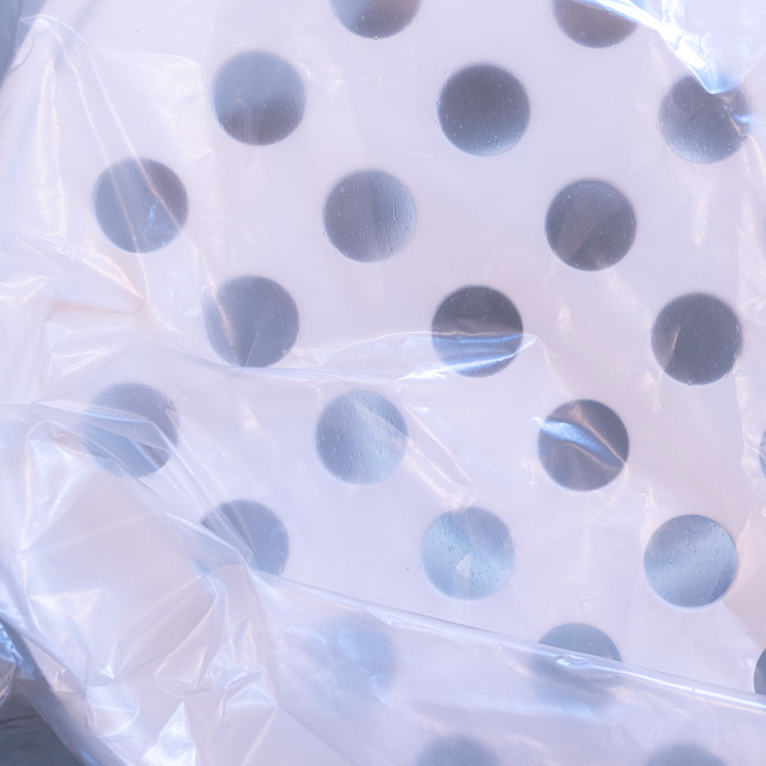 White circular item with gray polka dots, wrapped in clear plastic. Ideal for modern decor.