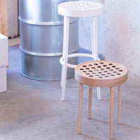 "White and natural wooden stools with round, perforated tops against a neutral background."