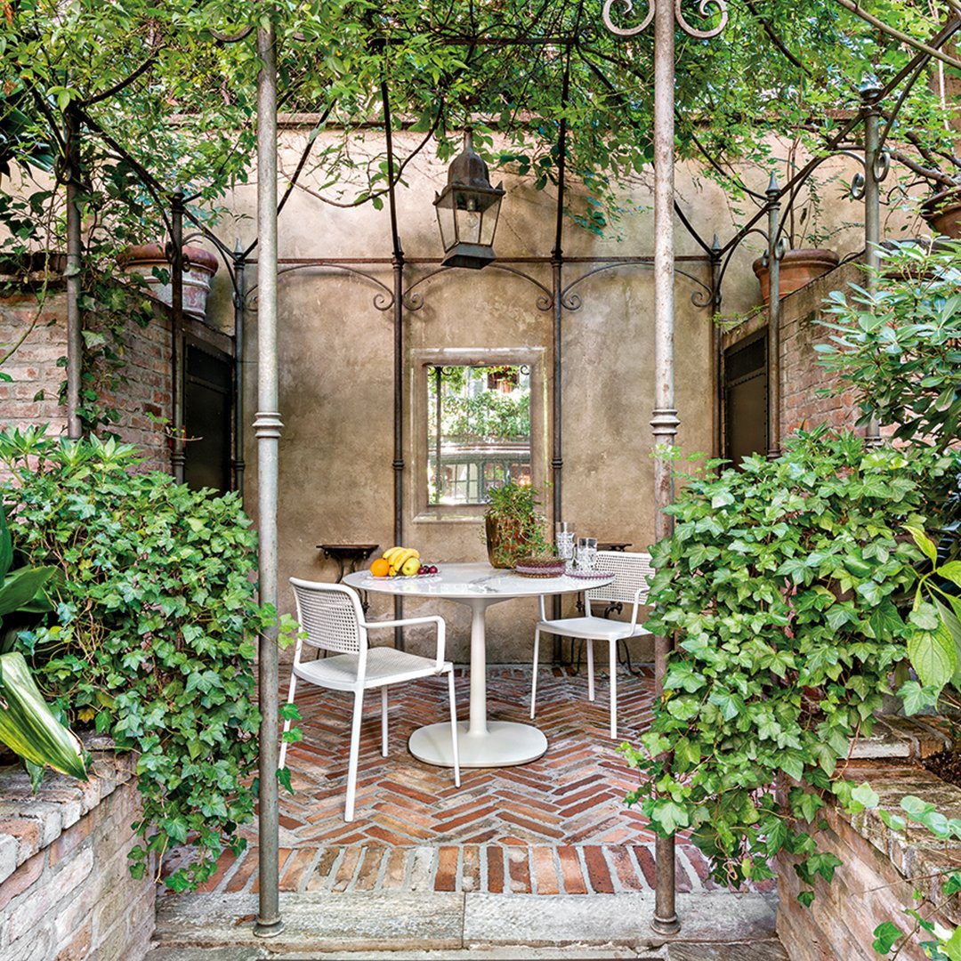 "Chic outdoor patio featuring white furniture, lush green foliage, and warm brick patterns for a cozy ambiance."