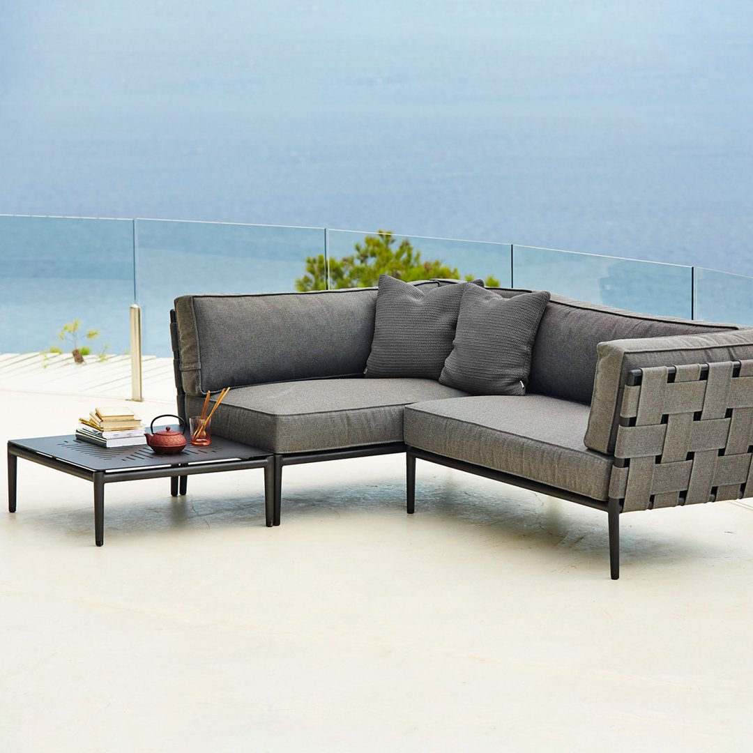Gray sectional sofa with woven accents and matching cushions, set against a serene blue ocean backdrop.