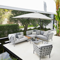 Gray wicker patio furniture set with white cushions and a large white umbrella, featuring a sleek, modern design.