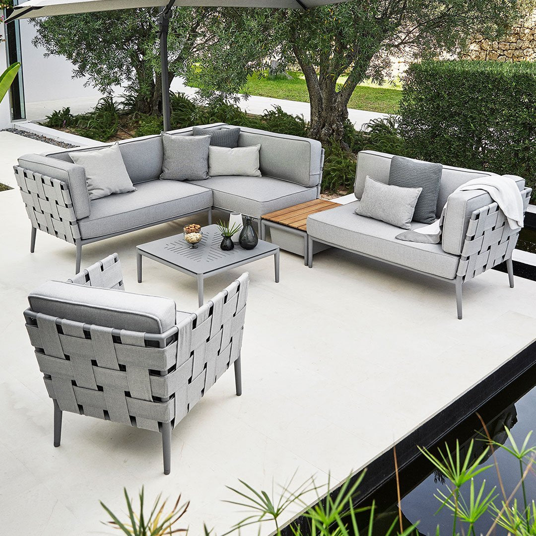 Modern gray outdoor sectional sofa with sleek lines and woven texture, complemented by neutral cushions and a wooden coffee table.