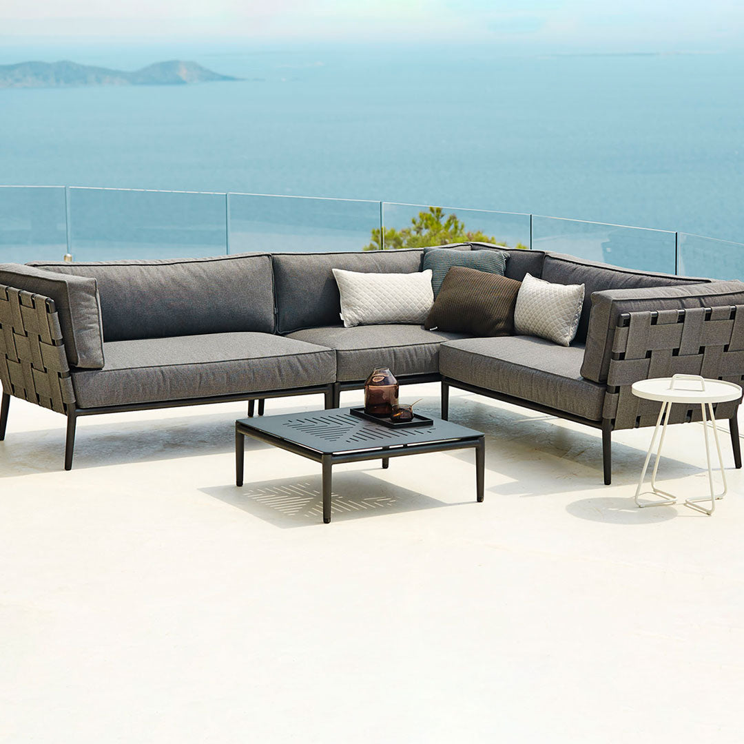 "Modern grey sectional outdoor sofa with textured patterns and neutral accent pillows against a scenic background."