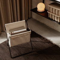 Beige canvas chair with black frame, set against a neutral backdrop with brown textures and soft lighting.